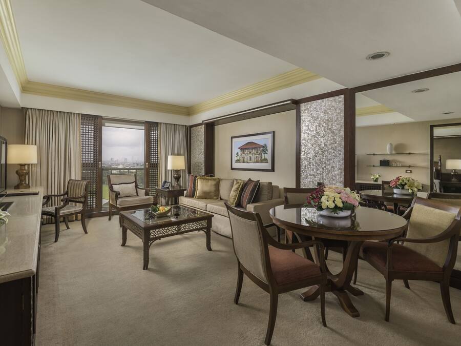 A hotel room with a living area, dining table, and a view of the city.