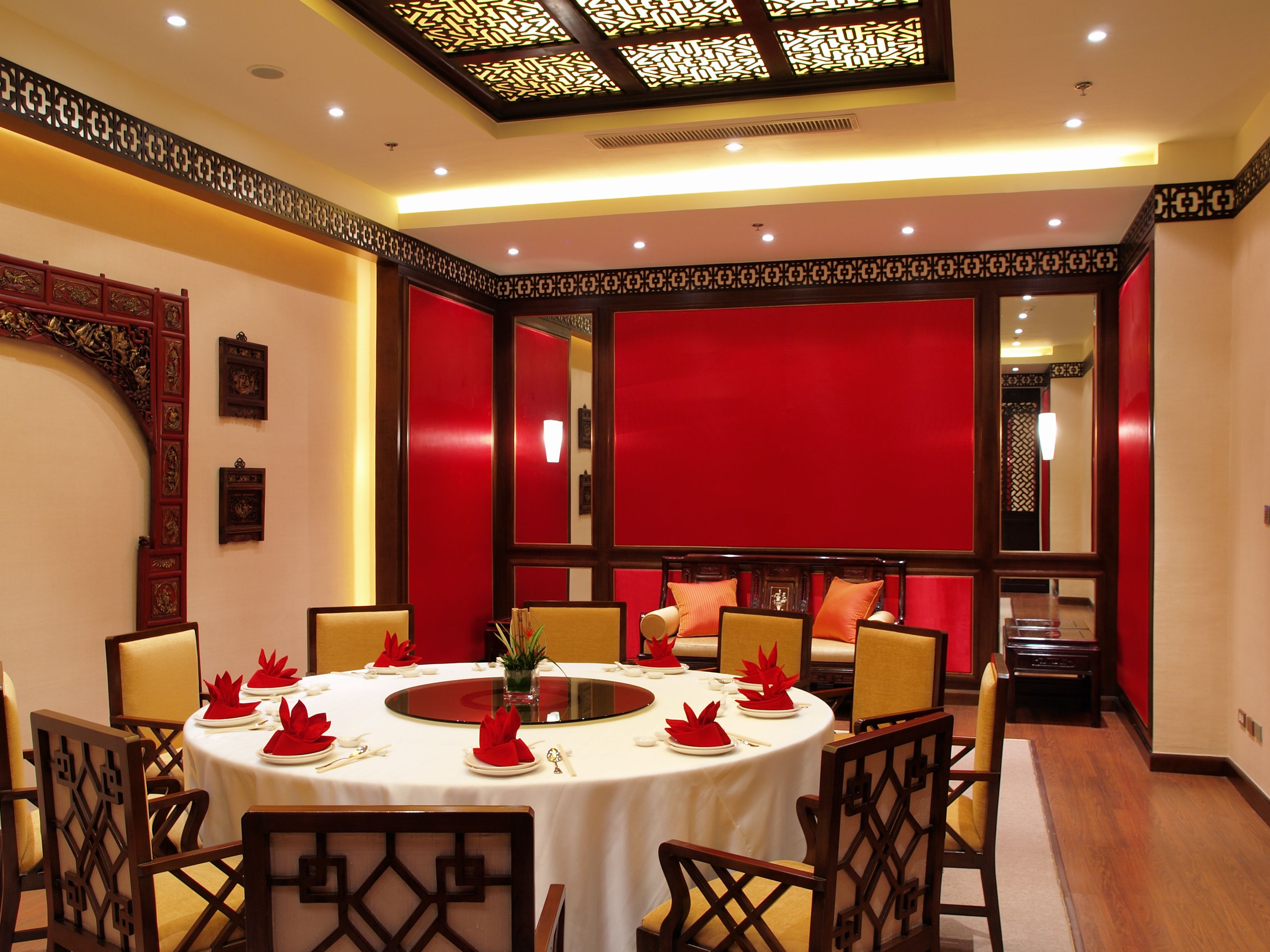 A round dining table with white tablecloth, red napkins, and gold accents.