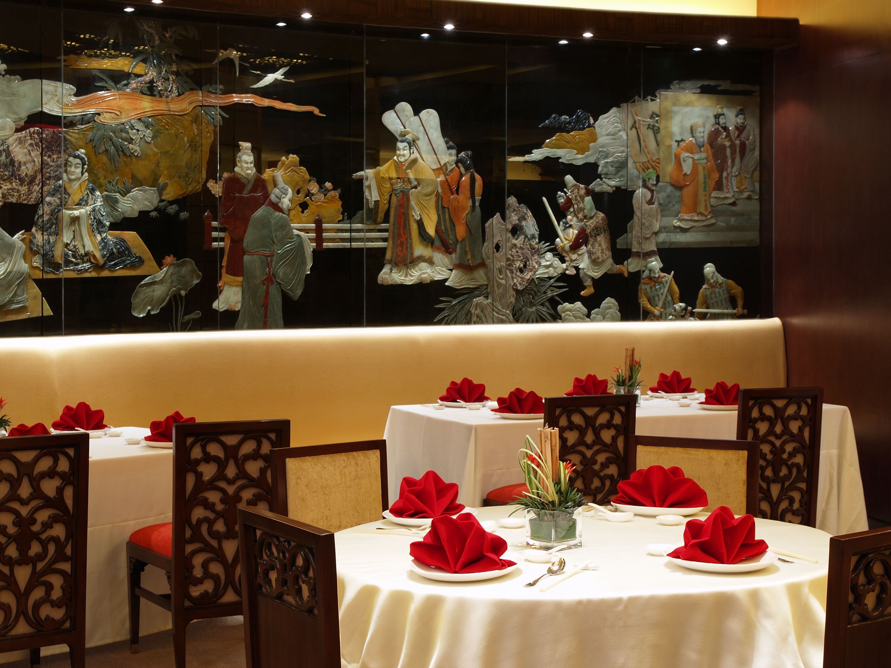 A restaurant with round tables set with white tablecloths, red napkins, and traditional Chinese artwork on the walls.