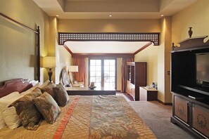 Amplia habitación de hotel con una cama grande, televisión y zona de estar con vistas al exterior.
