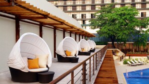 Un espace aménagé au bord de la piscine, avec des chaises blanches dotées de coussins et une terrasse en bois.