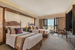 Habitación de hotel con dos camas, televisión, escritorio y vista a la ciudad.