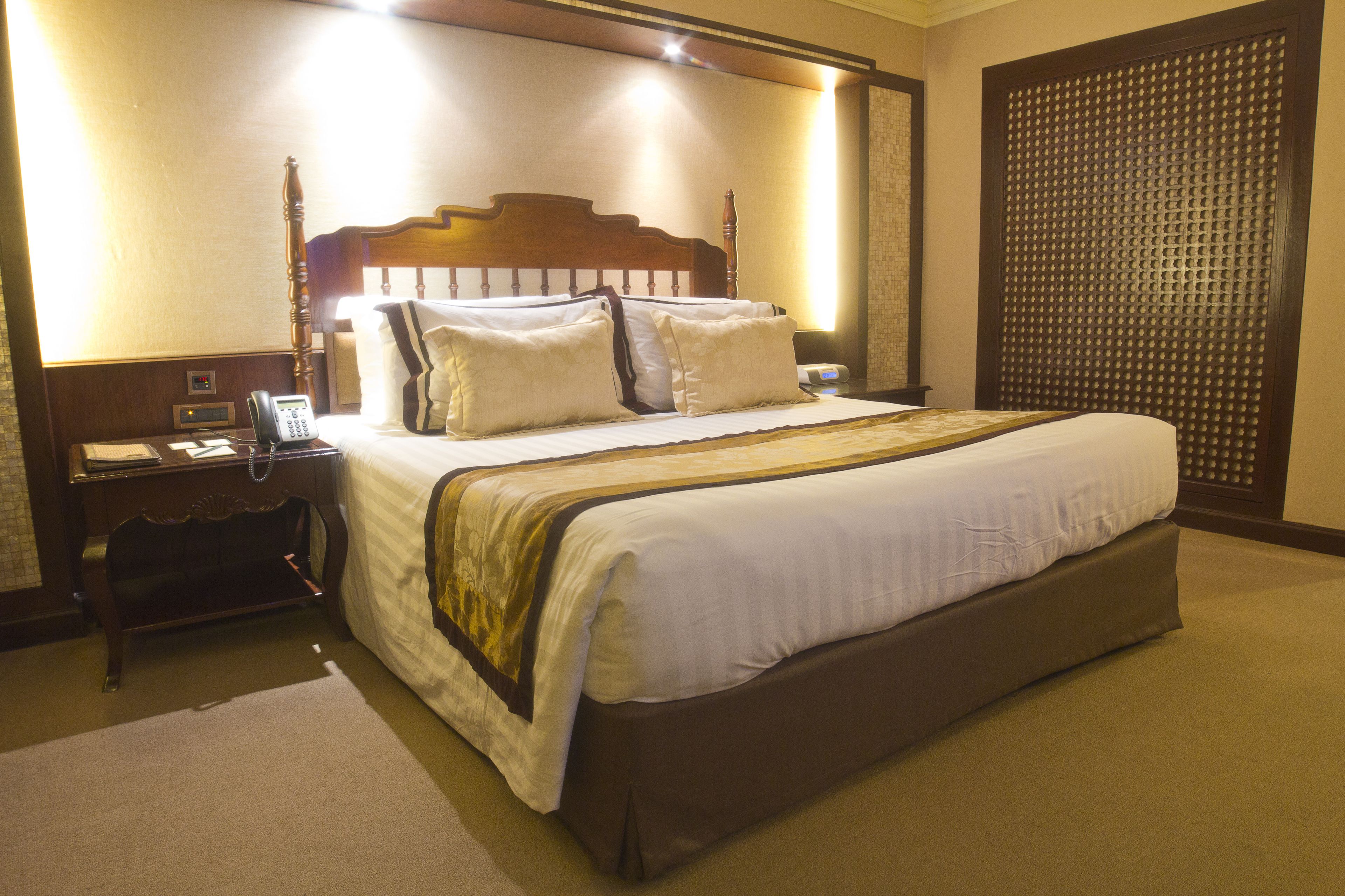 A hotel room with a large bed, a bedside table with a phone, and a wall-mounted light.