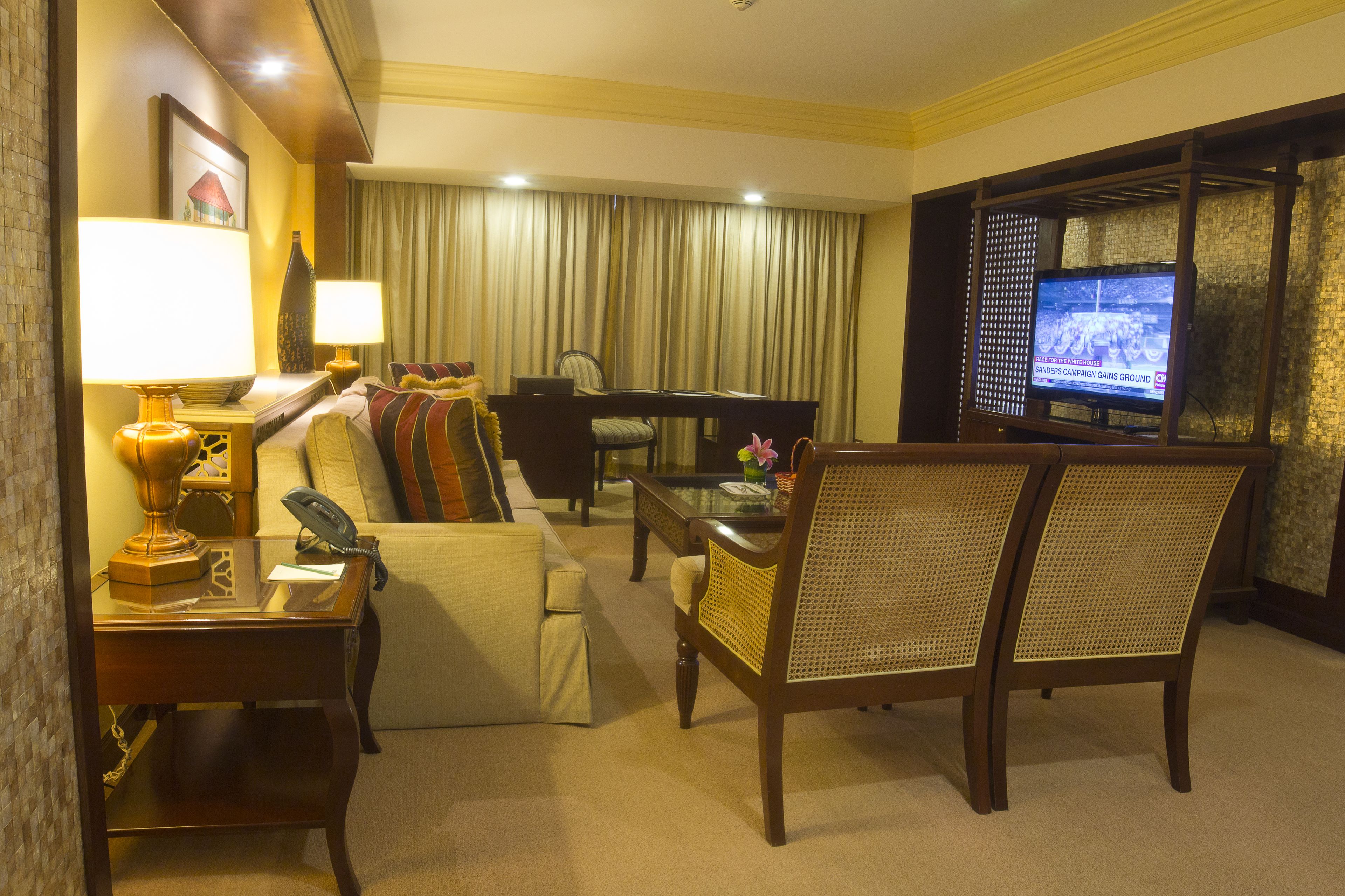 Habitación de hotel con sofá, escritorio con lámpara, televisión y una silla.