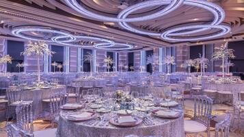 Un salón de banquetes con mesas redondas dispuestas para cenar, con sillas transparentes y vajilla.