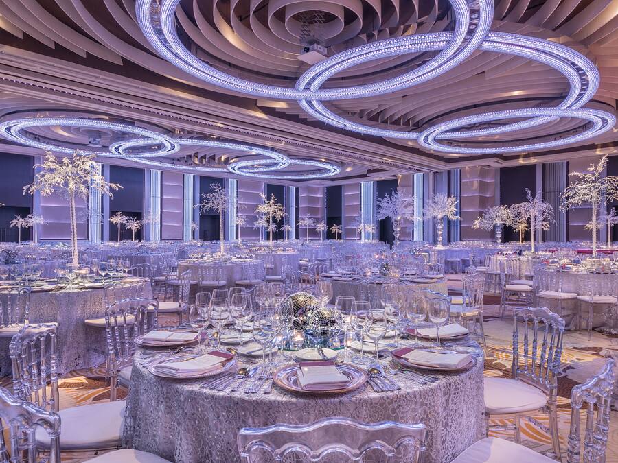A banquet hall with round tables set for dining, featuring clear chairs and table settings.