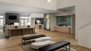Un vaste espace de vie doté d’un plancher en bois, d’un coin salon central avec un banc, d’une cheminée et d’une cuisine à l’arrière-plan.