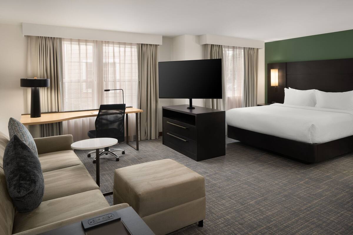 A hotel room with a bed, a desk with a TV, a sofa, and a chair.