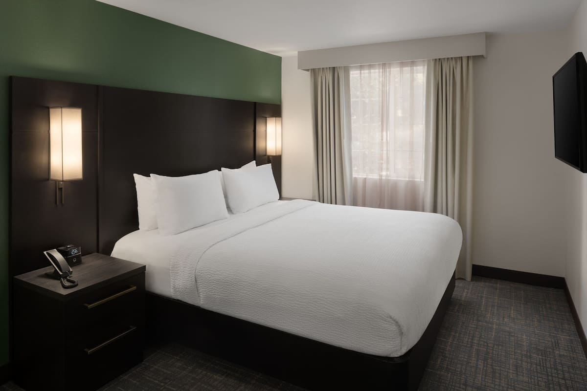 A hotel room with a large bed, a nightstand with a phone, and a window with curtains.