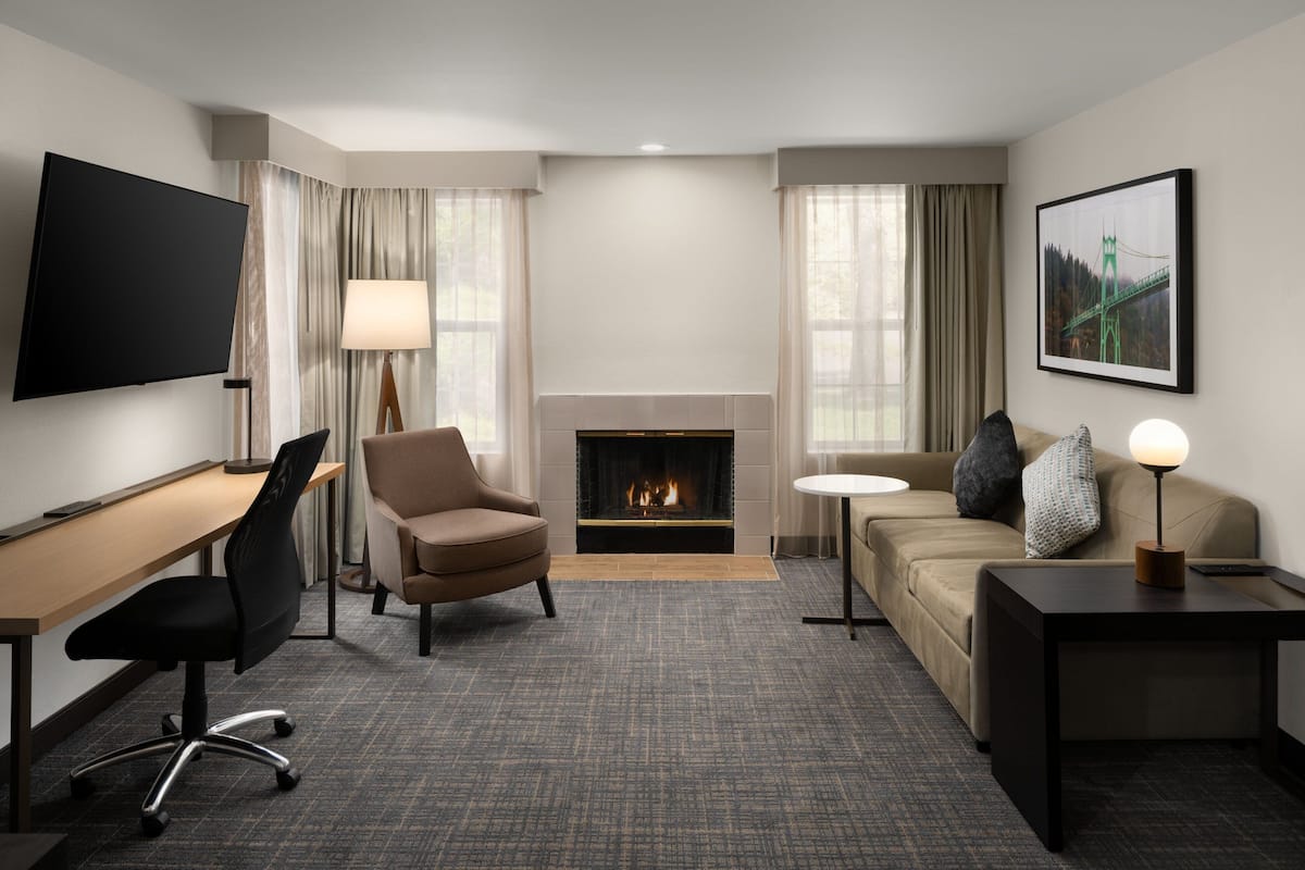 A hotel room with a flat-screen TV, a fireplace, a sofa, a desk, and a lamp.