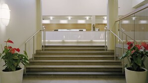 Eine Treppe führt zu einem Empfangsbereich mit einer Rezeption, Blumentöpfen und einem modernen Design.