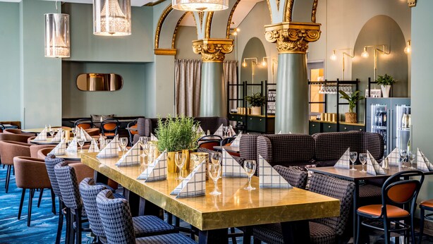 Ein Restaurant mit einem langen Tisch, bequemen Sitzgelegenheiten und dekorativer Beleuchtung.