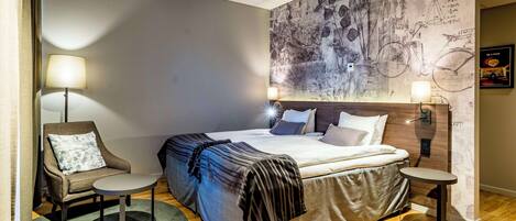 A modern hotel room with a large bed, a chair, a small table, and a wall mural.