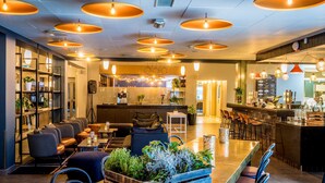 Eine moderne Hotellobby mit Barbereich, Sitzgelegenheiten und einer sichtbaren Küche im Hintergrund.