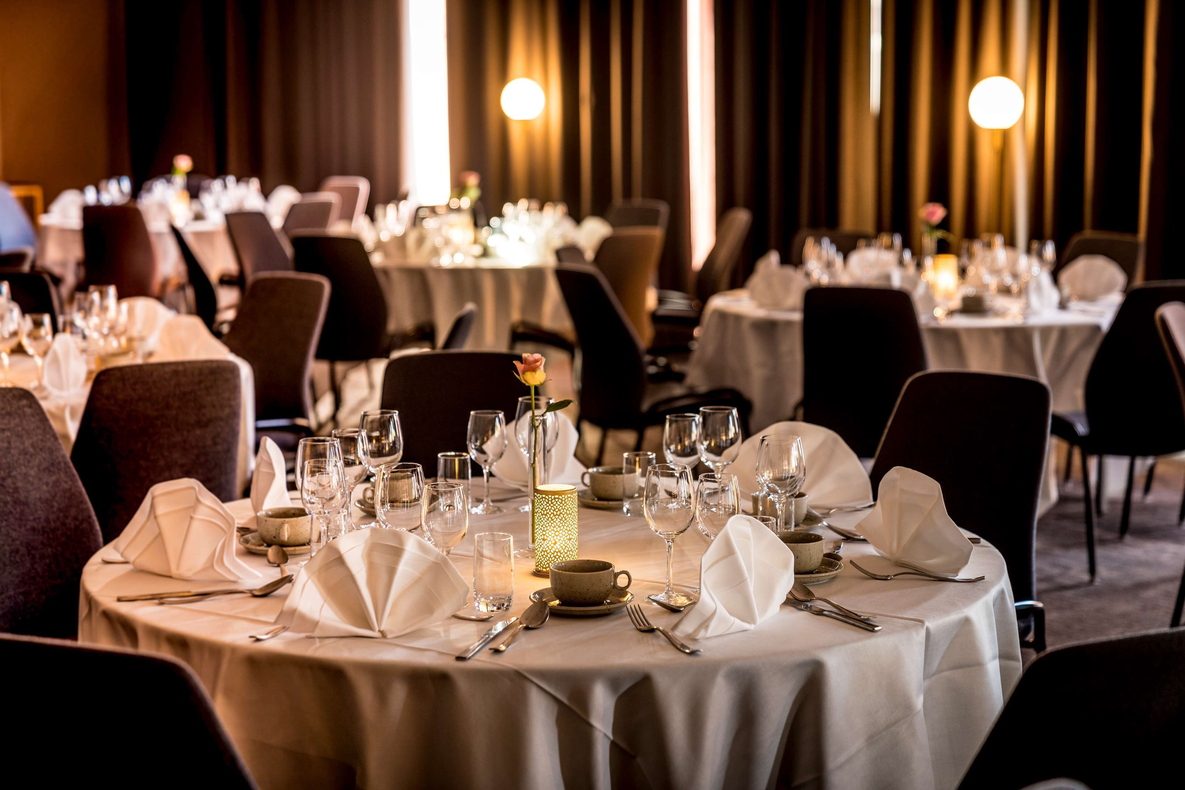A restaurant with round tables set for dining, featuring white tablecloths, glassware, and candles.