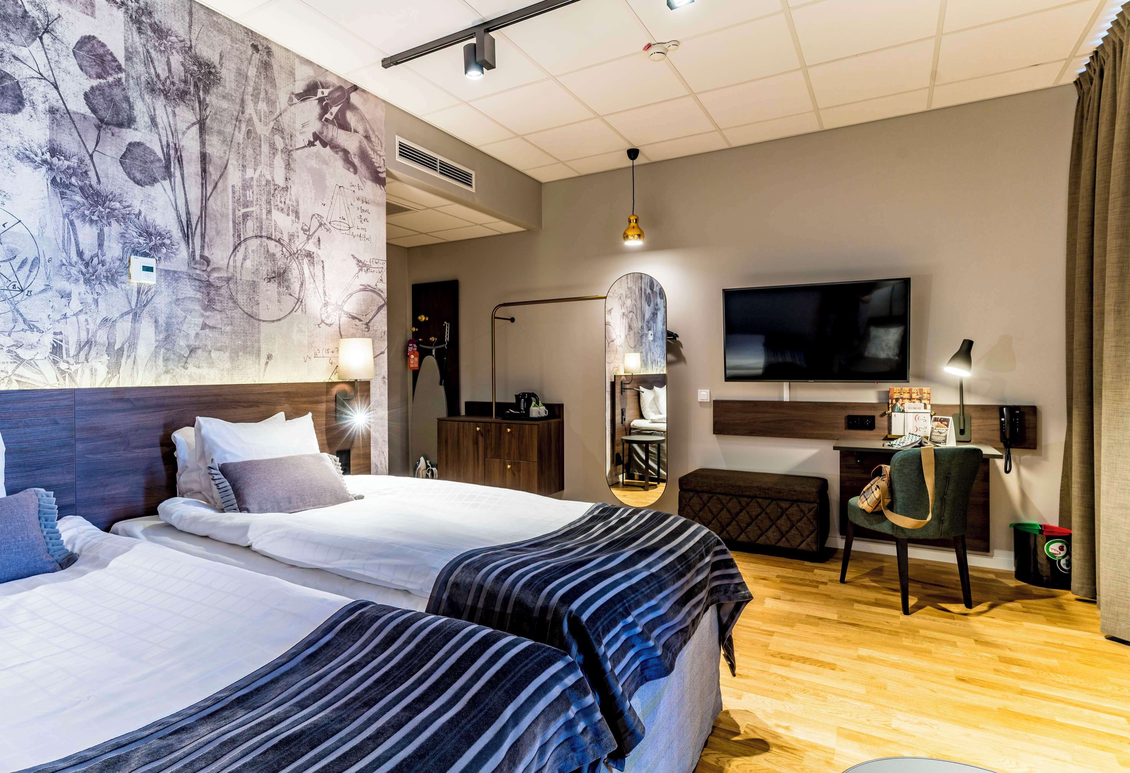 A hotel room with two beds, a TV, a desk, and a mirror.