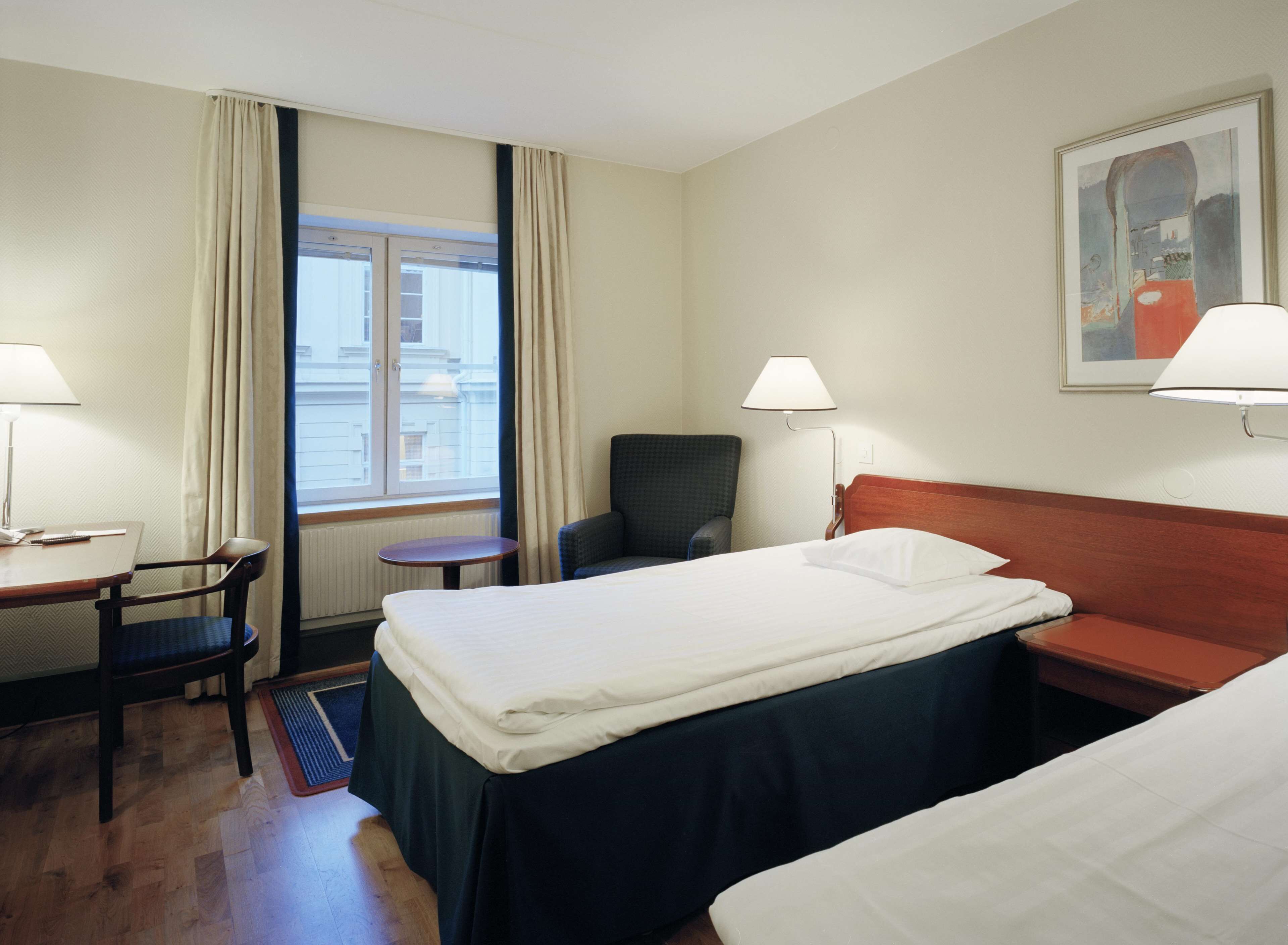 Una habitación de hotel con cama, una silla, una mesa y un ventanal con cortinas.