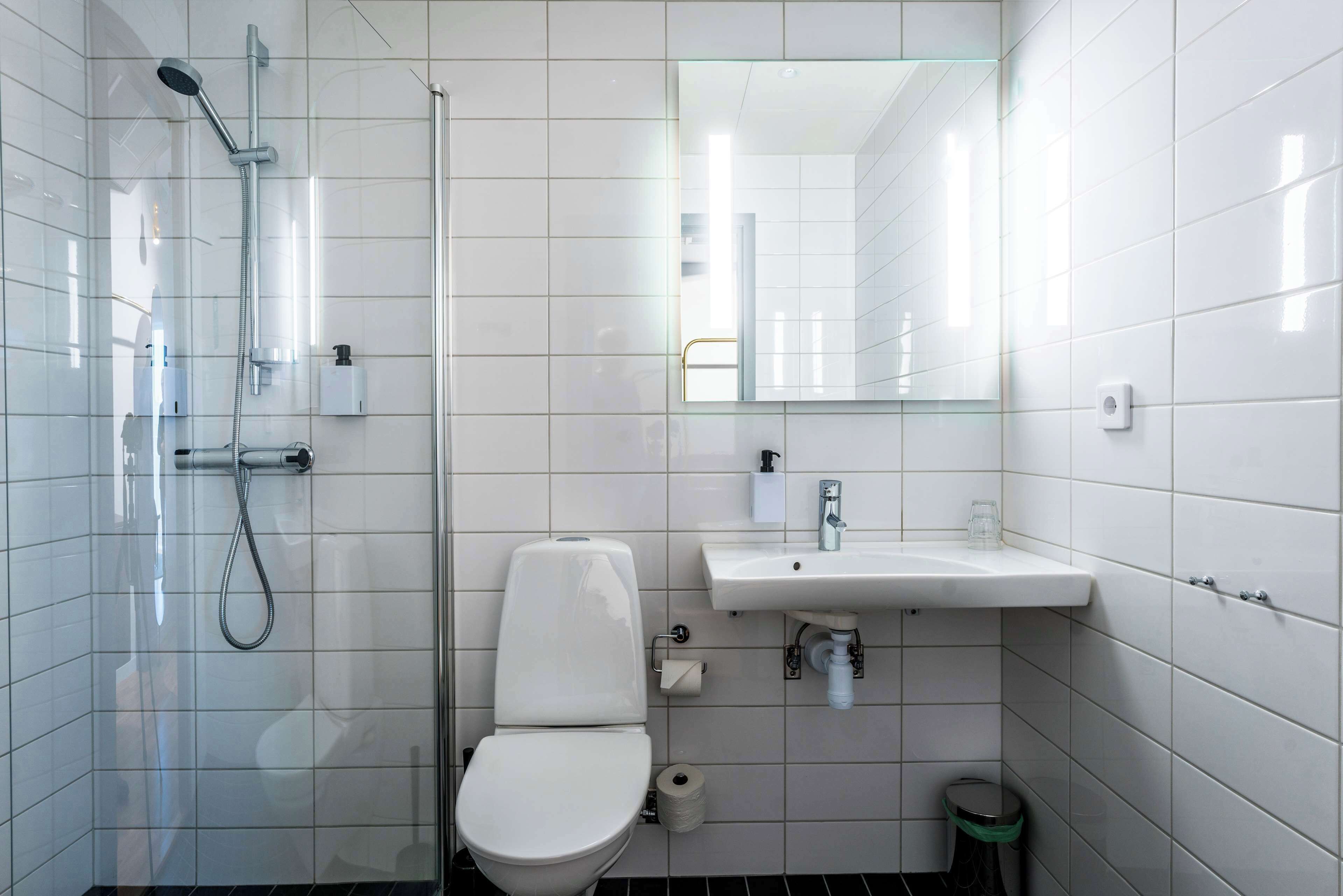 Un baño moderno con ducha de vidrio, inodoro blanco, lavamanos con espejo y un cubo de basura.