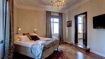 A spacious bedroom with a large bed, a chandelier, and a television on the wall.