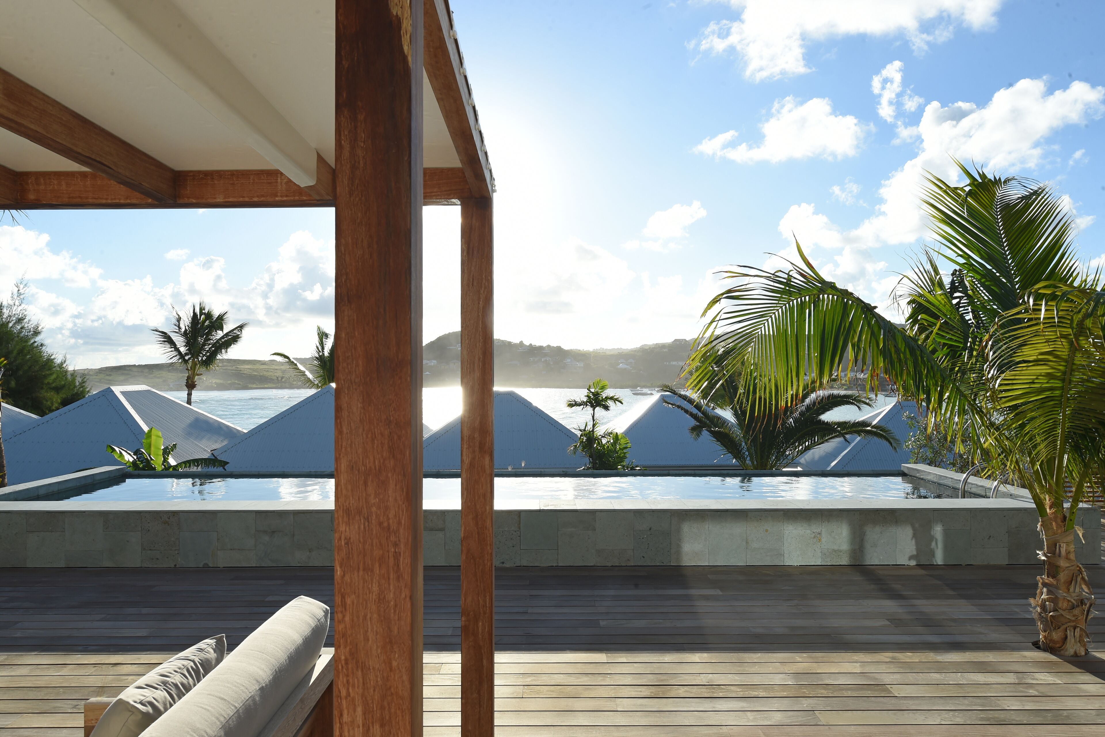 A pool area with a wooden deck, lounge chairs, and a view of the ocean and hills.