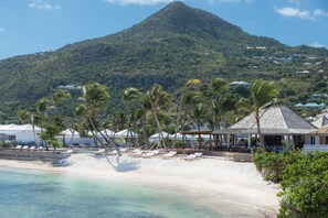 A beach resort with lounge chairs, a gazebo, and a mountain in the background. - Le Sereno (St. Barthelemy)