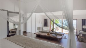 A modern hotel room with a large bed, a sitting area with a sofa and coffee table, and a balcony with a view of greenery. - Le Sereno (St. Barthelemy)