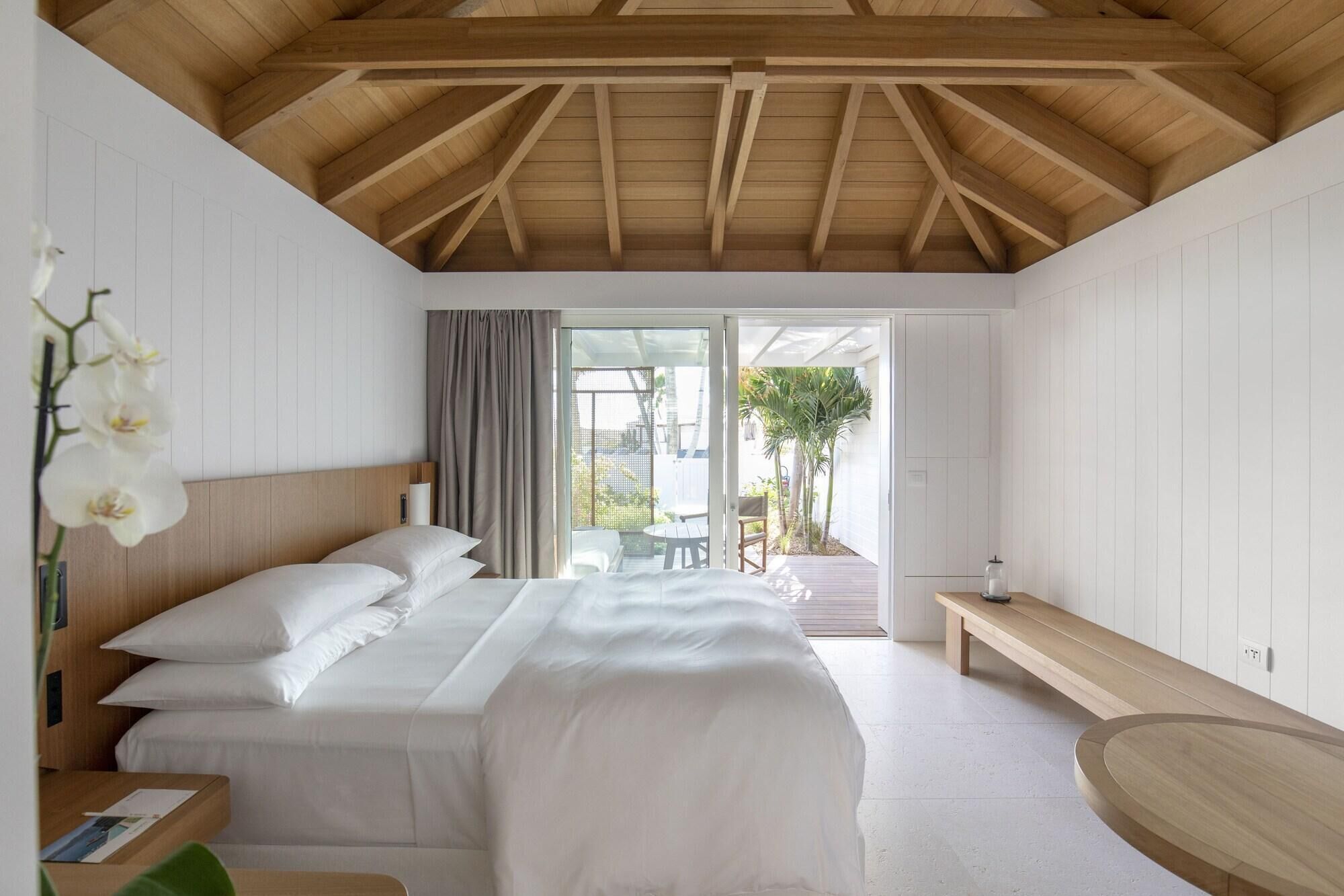 A bedroom with a bed, a bench, a table, and a view of the outdoors.