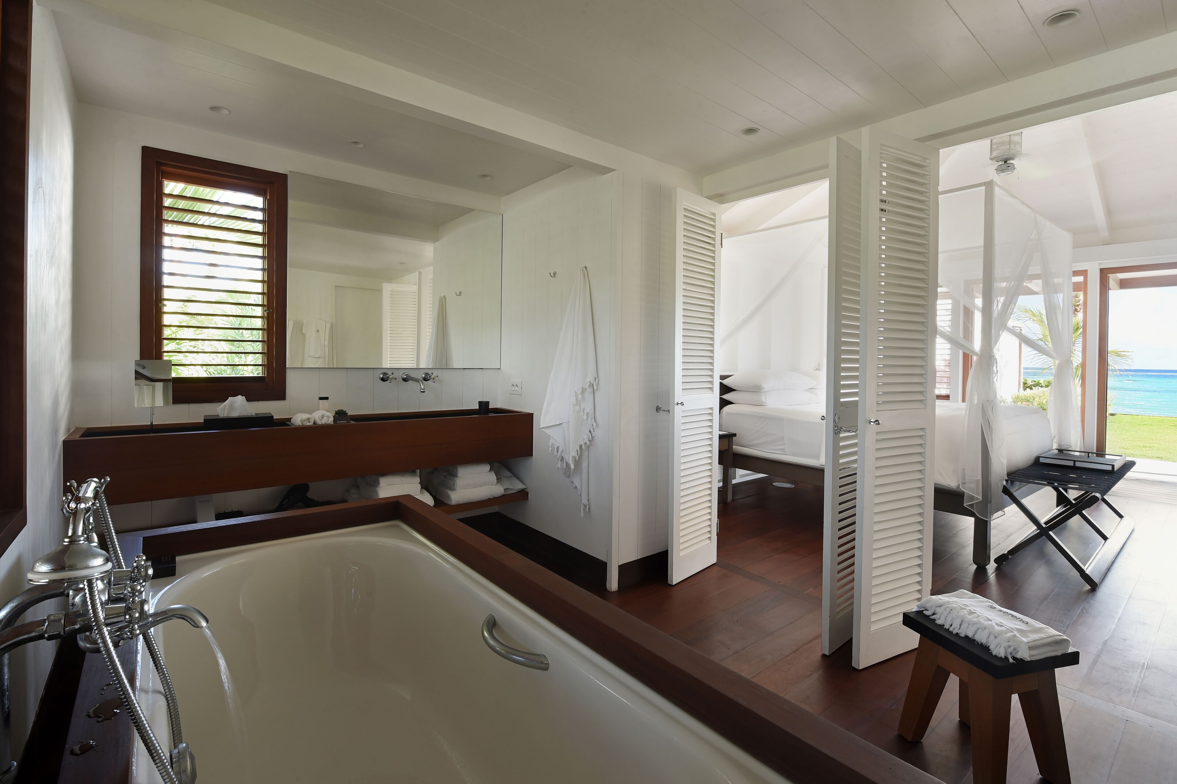 Een moderne badkamer met een bad, een grote spiegel en uitzicht op de oceaan door een geopende deur.