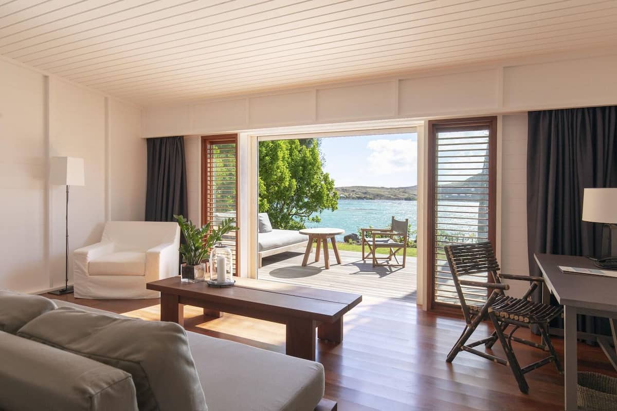 A modern room with a sofa, a coffee table, and a desk. There is a view of the sea through large windows.