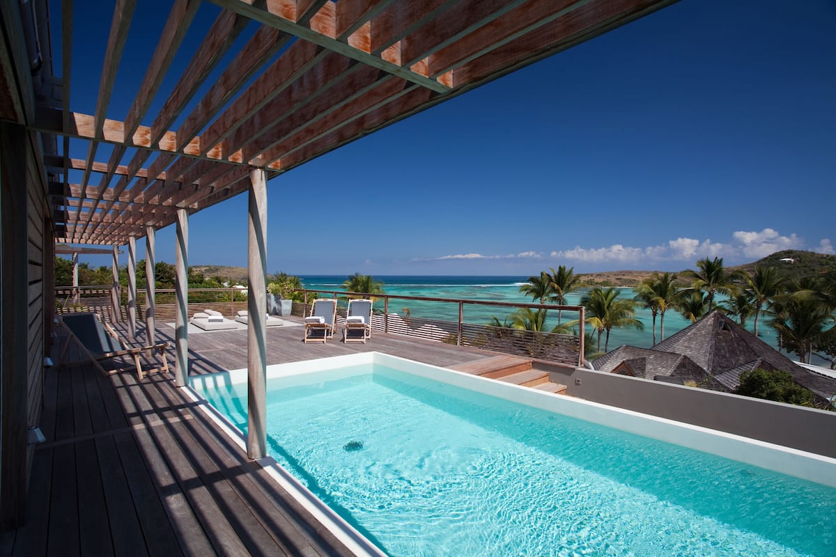 A wooden deck with a pool, lounge chairs, and a view of the ocean.