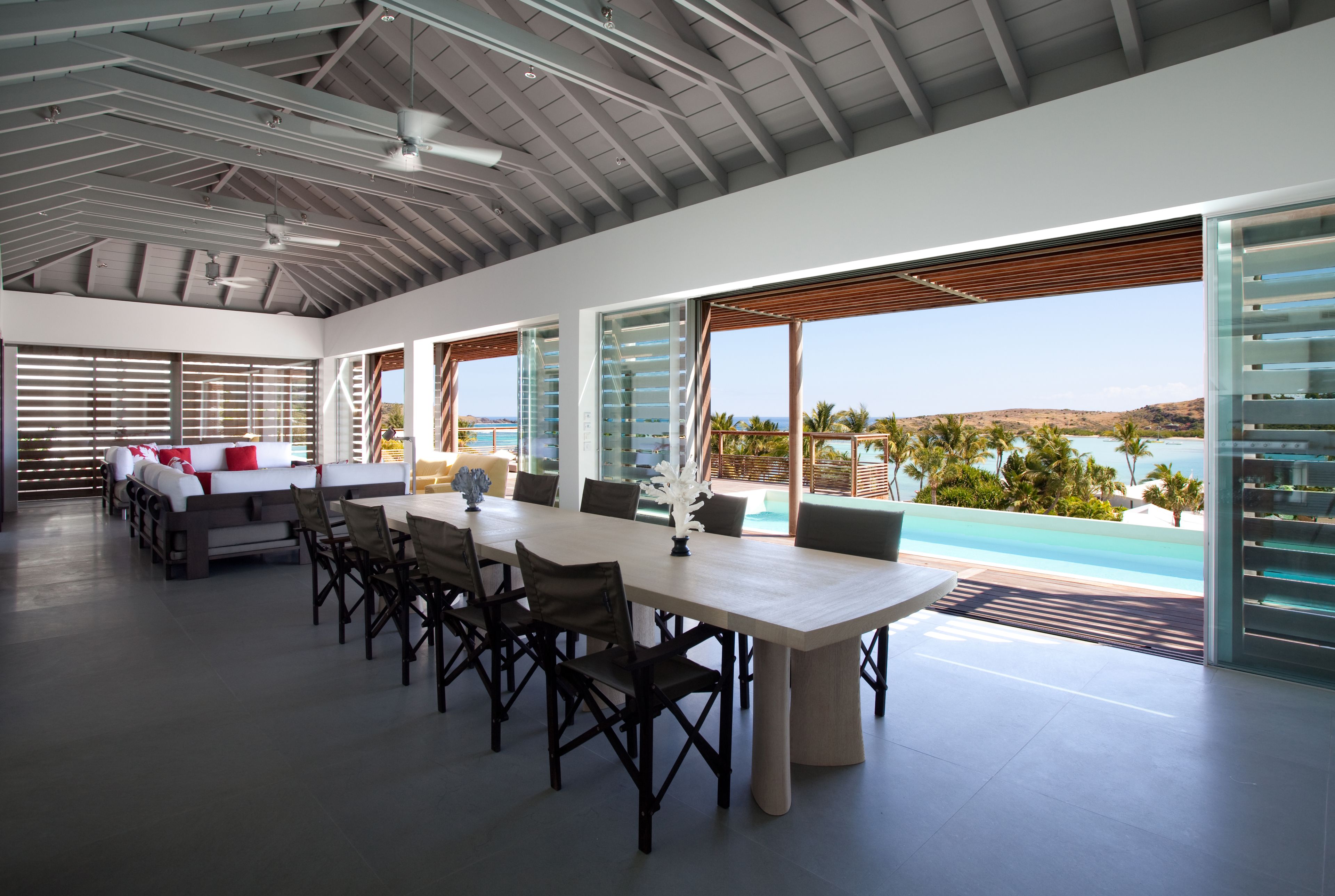 A spacious dining area with a large table and chairs, large windows with blinds, and a view of a pool and mountains.