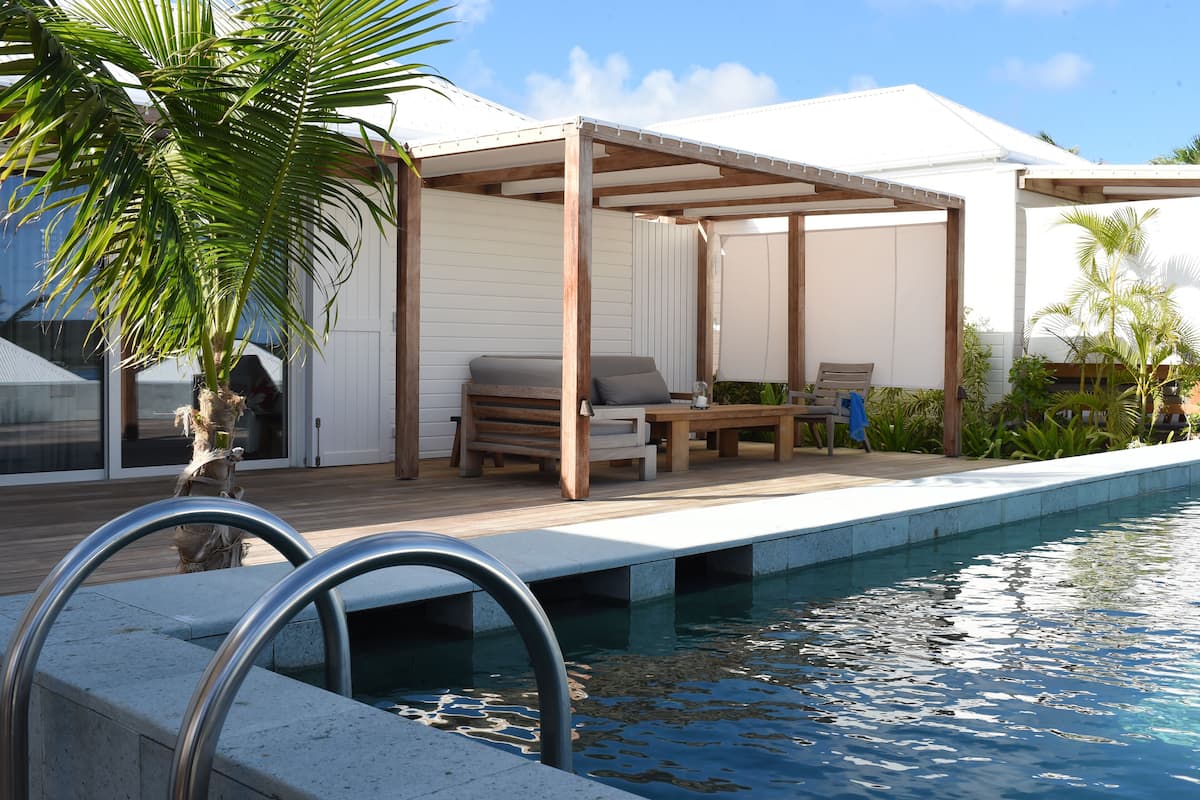 A pool area with a wooden deck, lounge chairs, and a covered seating area.