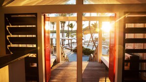 A wooden deck leading to a beach with palm trees and a sunset view. - Le Sereno (St. Barthelemy)