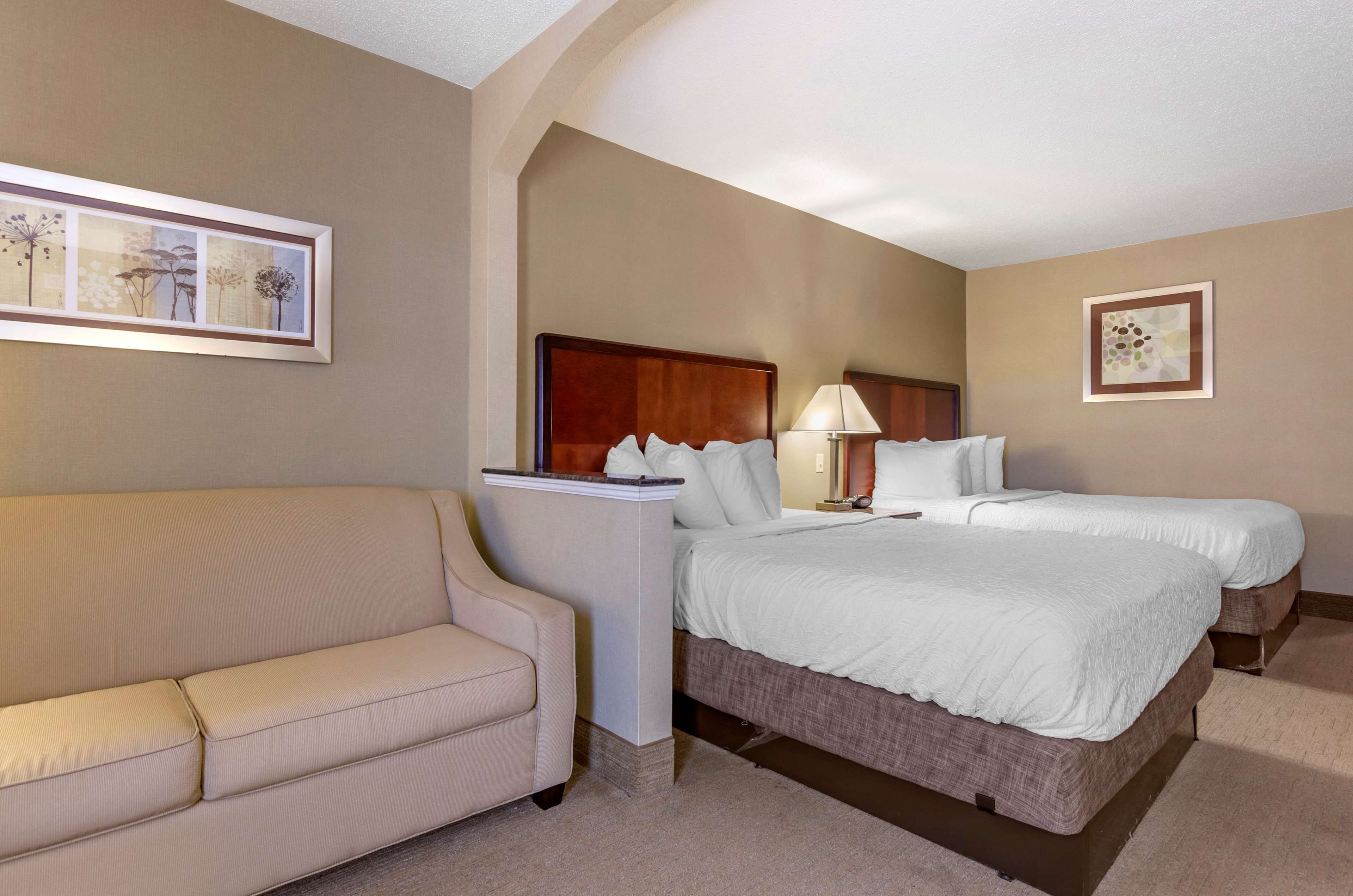 A hotel room with a bed, a bedside table with a lamp, a sofa, and framed artwork on the walls.