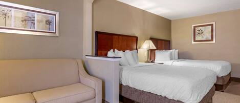 A hotel room with a bed, a bedside table with a lamp, a sofa, and framed artwork on the walls.