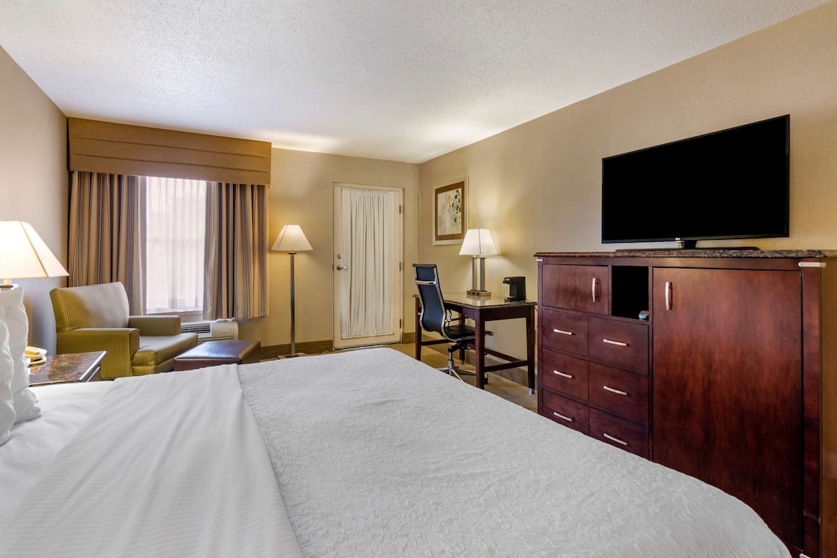 A hotel room with a large bed, a desk with a chair, a television, and a wardrobe.