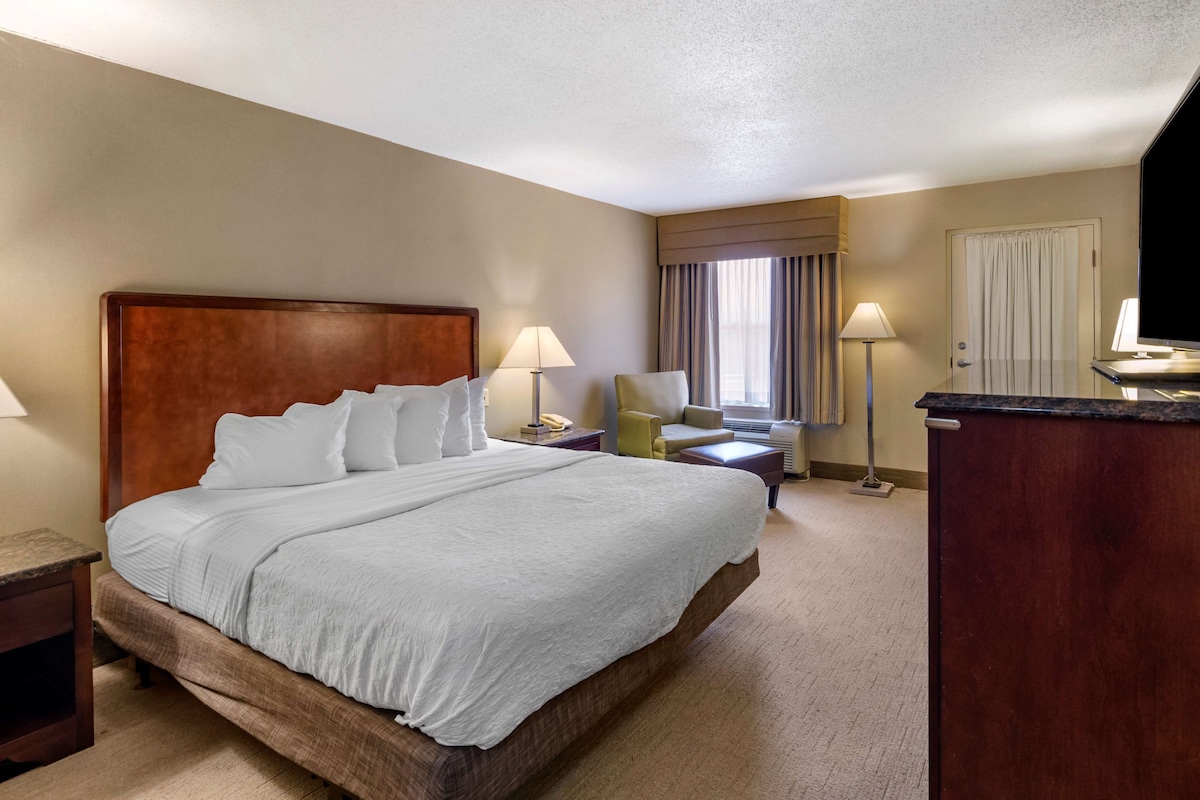 A hotel room with a large bed, two bedside tables, a desk, a chair, and a TV.