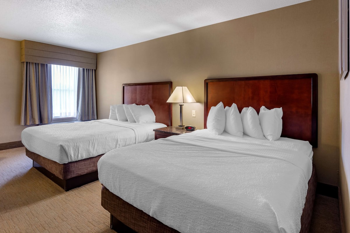 Two double beds with wooden headboards, a bedside table with a lamp, and a window with curtains.