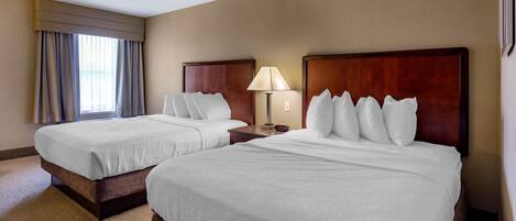 Two double beds with wooden headboards, a bedside table with a lamp, and a window with curtains.