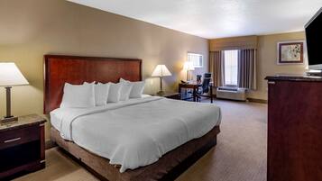 A hotel room with a large bed, two bedside tables with lamps, a desk with a chair, a flat-screen TV, and a window with curtains.