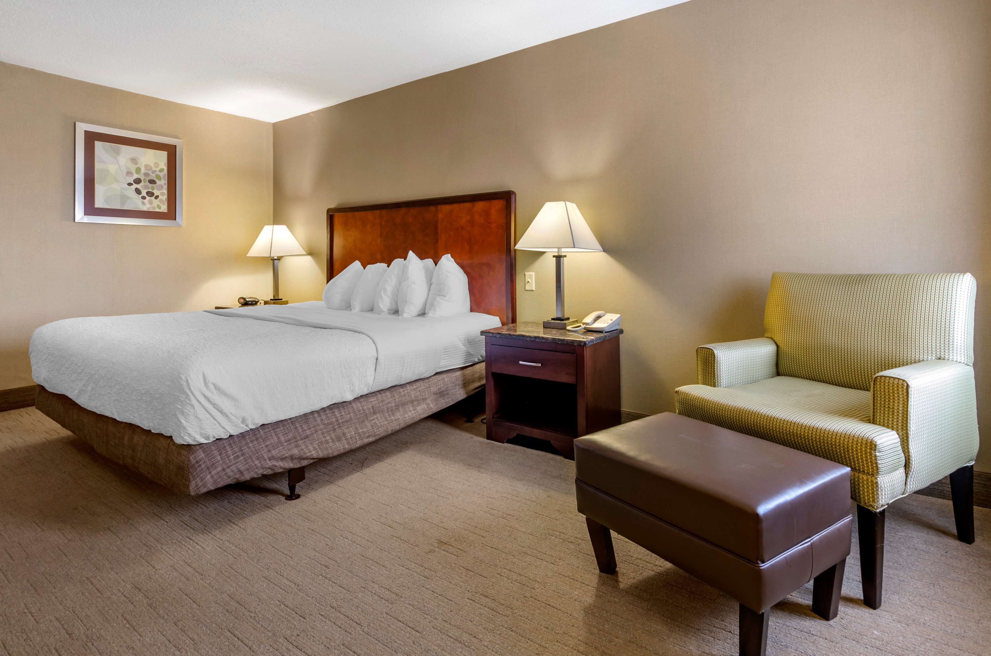 Een hotelkamer met een groot bed, twee nachtkastjes met lampen, een stoel en een klein tafeltje.