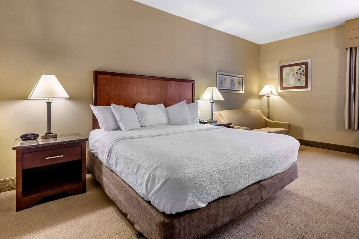 A hotel room with a large bed, two bedside tables, a nightstand, a chair, and a wall-mounted lamp.