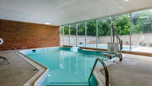 An indoor swimming pool with clear glass walls, a brick wall, and a view of a backyard with a picnic table and a fence.