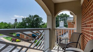 A balcony with a view of a brick building and a parking lot.