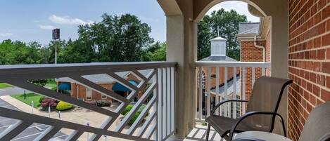 A balcony with a view of a brick building and a parking lot.