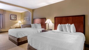 A hotel room with two beds, a wooden headboard, a nightstand with a lamp, and a framed picture on the wall.