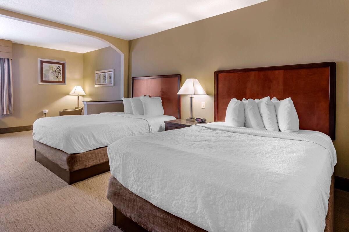 A hotel room with two beds, a wooden headboard, a nightstand with a lamp, and a framed picture on the wall.