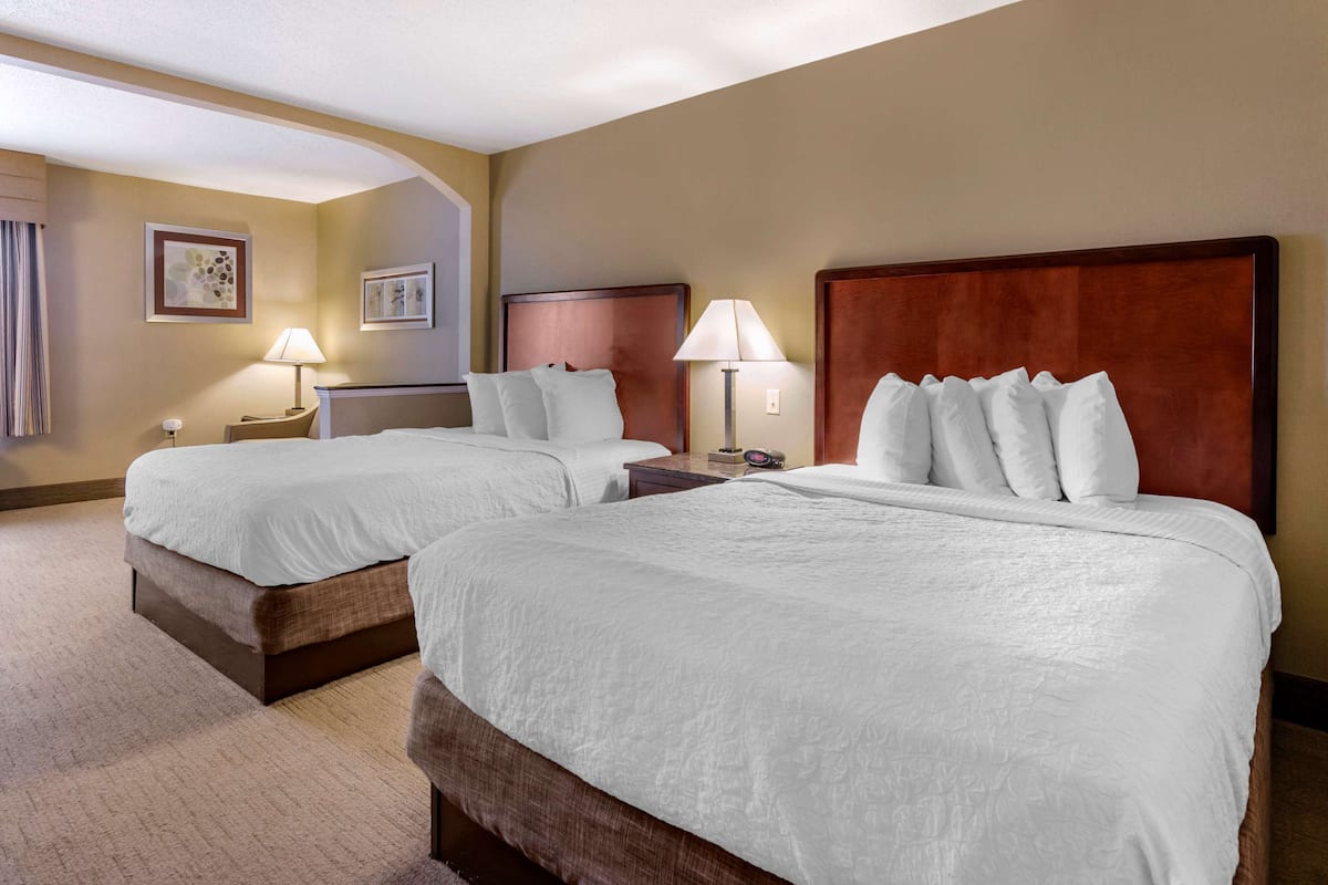 A hotel room with two beds, a wooden headboard, a nightstand with a lamp, and a framed picture on the wall.