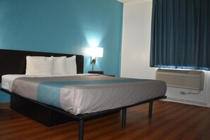 A hotel room with a bed, a nightstand, a lamp, a window with curtains, and an air conditioning unit. - FairBridge Inn Express Melrose Park (Melrose Park)