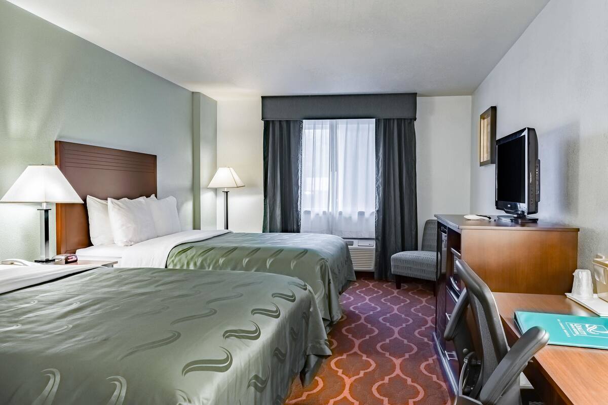A hotel room with two beds, a desk, a chair, a television, and a window with curtains.